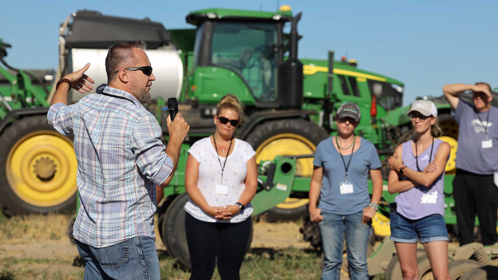 Small group listening to speaker with agriculture tractor in background