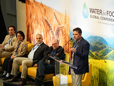 Small group sitting on stage beside person speaking in podium.