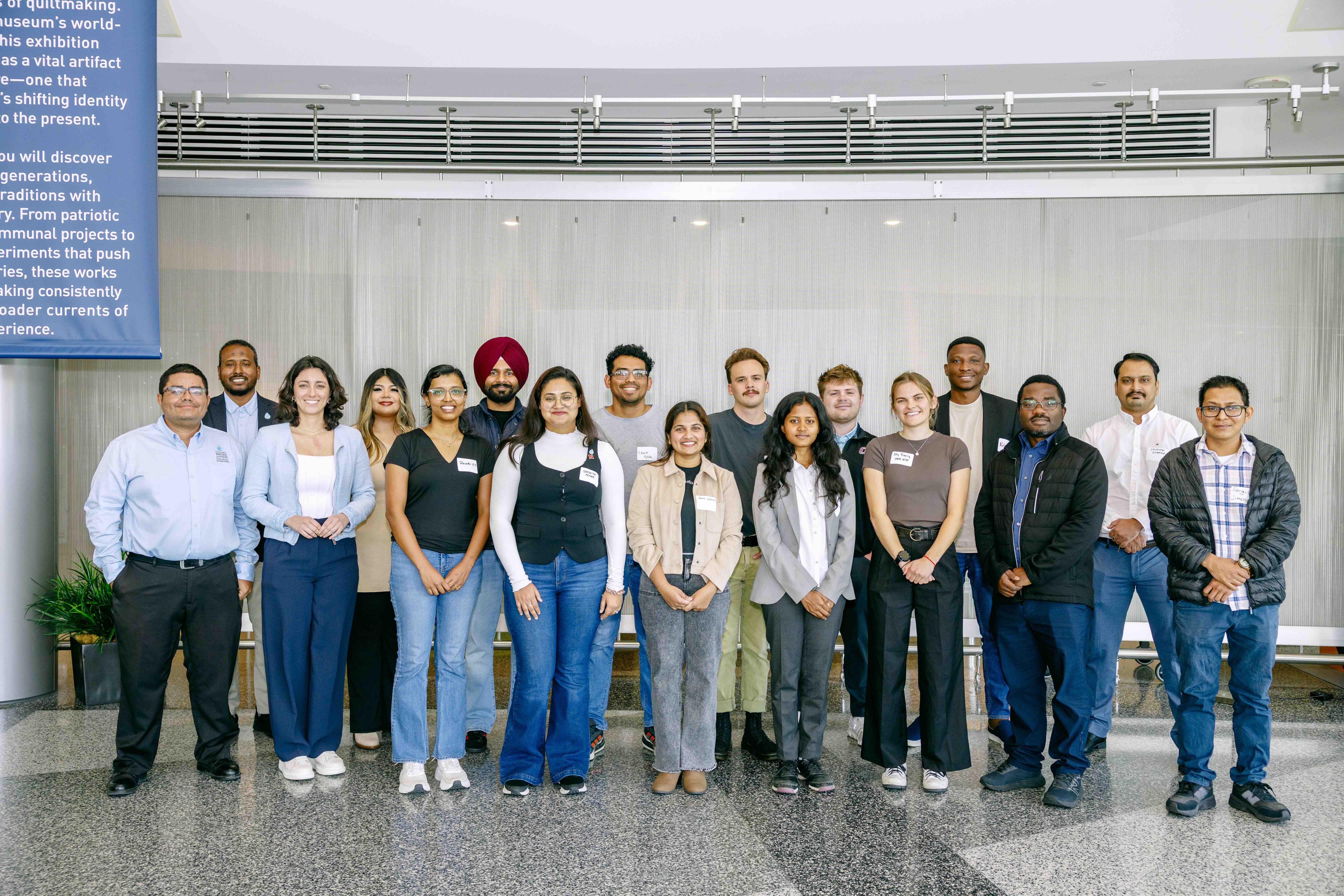 Group photo of about 15 people wearing name tags, standing in a lobby in front of a light-colored wall.