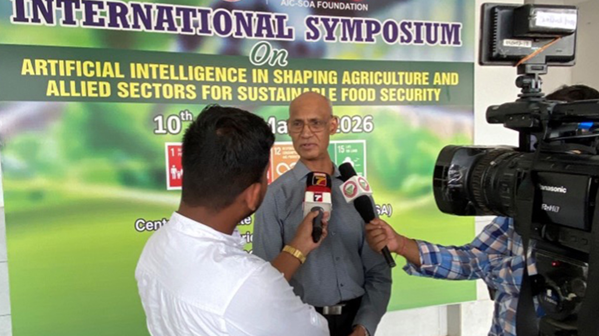 Interview in front of a conference banner about artificial intelligence in agriculture and sustainable food security, with microphones and a video camera pointed at the speaker.
